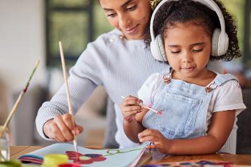Mother and daughter bonding in painting activity with girl wearing headphones for autism help