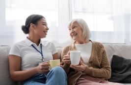Social worker having tea and chatting with senior woman in living room