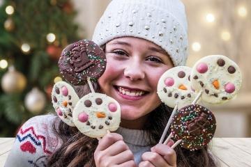 Female wearing winter jumper and hat holding festive lollipops